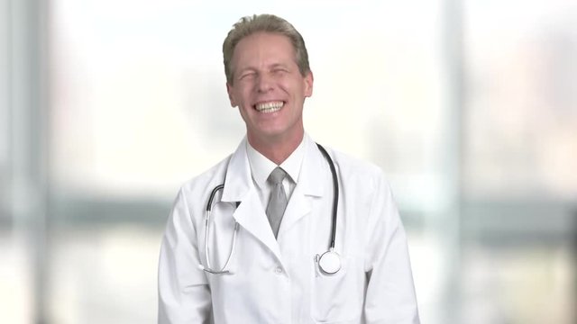 Mature doctor laughing on blurred background. Middle-aged male doctor in white coat is laughing. Joyful middle-aged doctor.