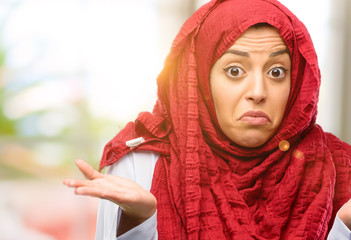 Young arab woman wearing hijab doubt expression, confuse and wonder concept, uncertain future shrugging shoulders