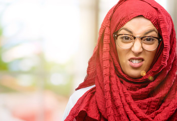 Young arab woman wearing hijab angry and stressful frowns face in dissatisfaction, irritated and annoyed, expressing anger