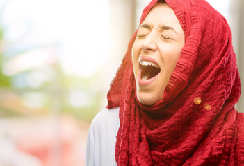 Young arab woman wearing hijab stressful, terrified in panic, shouting exasperated and frustrated. Unpleasant gesture. Annoying work drives me crazy