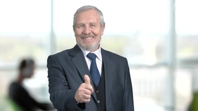 Senior bearded businessman showing thumb up. Joyful elderly man in formal wear giving thumb up on office background. Symbol of successs.