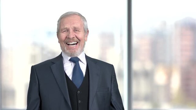 Laughing businessman on blurred background. Senior male executive in business suit laughing on window city background.