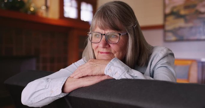 Close-up of content mature woman relaxed on sofa daydreaming inside home, Smiling carefree senior woman looking thoughtful with head rested on hands sitting on living room couch, 4k