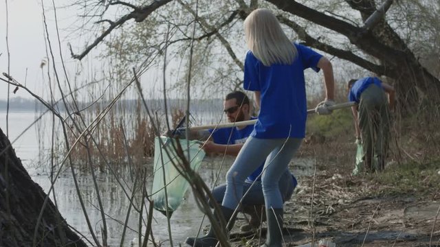Man and woman in t-shirts of volunteer community taking care of forest ecology cleaning up trash on pond.