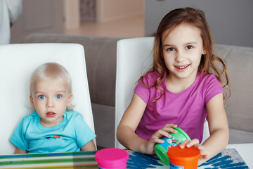 Two happy children Blond boy and girl playing sitting at table at home