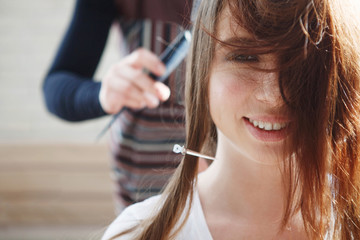 A professional stylist works with the long hair of a young beautiful girl.