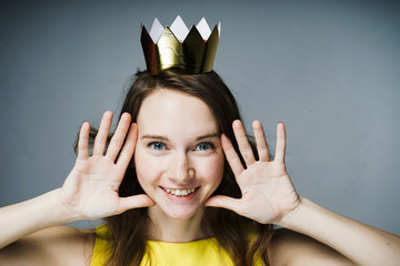 happy blue-eyed girl in a yellow dress smiles, on her head a golden crown