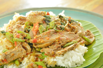 spicy fried duck meat curry with basil leaf and rice on fresh banana leaf