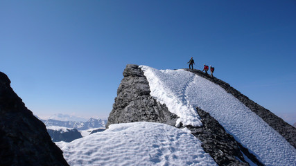 mountain guide and two clients heading to a high mountain peak and reaching the top under a blue sky