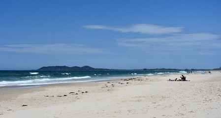 Fototapeta na wymiar Byron beach in sunny afternoon with blue sky in Byron Bay, Australia. People relaxing on the beach.