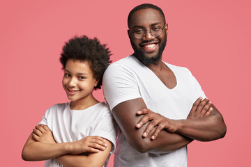 Smiling happy dark skinned young male and African American teenager stand back to each other, keep hands crossed, express positive emotions, have confident expressions, rejoice having spare time.