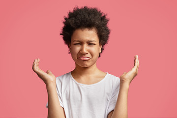 Image of discontent unhappy crying small kid with Afro hairstyle, feels frustrated and upset as punished by parents for being naughty, curves lower lip and gestures, isolated over pink background - Powered by Adobe