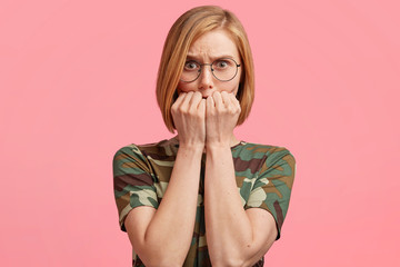 People and negative feelings concept. Nervous beautiful female with stylish haircut, bites finger nails and looks frustrated, anxious, dressed casually, worries before first date or important exam.