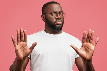 Photo of serious young African American male denies something, expresses his refusement, poses against pink background, rejects participaiting in discussion, has confident look. I don`t want it!