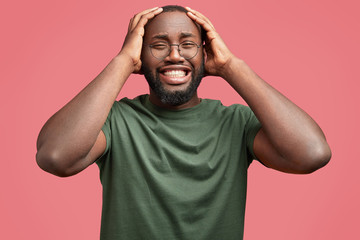 Sorrowful dark skinned male cries as being in depression, has big grief in life and unhappy expression, dressed in casual t shirt, isolated over pink background. African man has serious problem