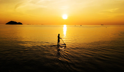 Aerial: Sunset silhouette of a person standing up at paddle board on vacation in Thailand
