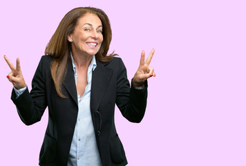 Middle age business woman looking at camera showing tong and making victory sign with fingers