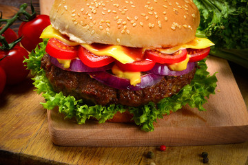 Delicious tasty burger with beef, tomatoes, salad and sauce on wooden table and black background.  Space for text or design.