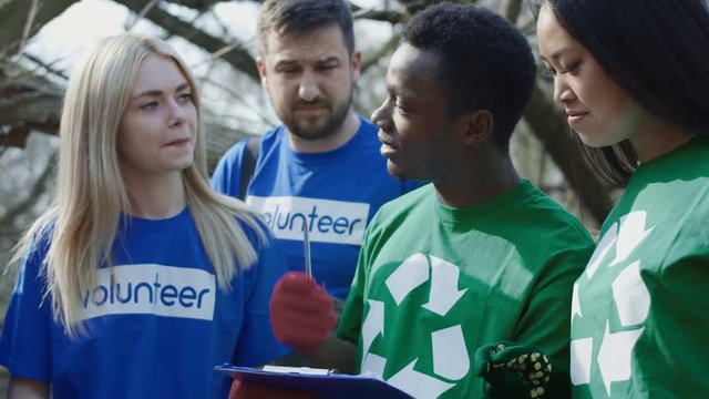 Close view of diverse cheerful volunteers preparing for cleanup of woods. The coordinator allocates responsibilities and identifies areas for cleaning.
