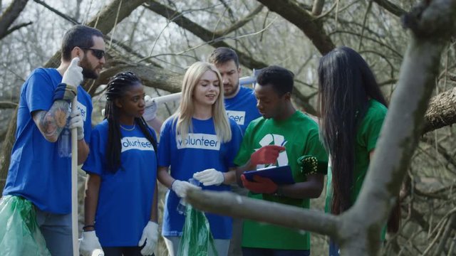 Multiethnic people in group of volunteer community standing in forest wearing colorful t-shirts and talking to coordinator they determine the location for cleaning and the amount of work.