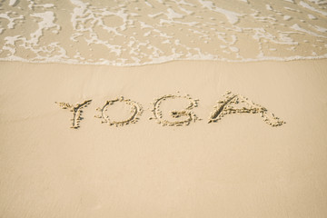 The inscription on the sand `Yoga`. Beach and waves.