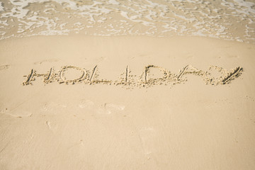 The inscription on the sand "Holiday". Beach and waves.