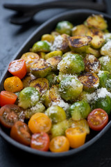 Close-up of pan fried brussels sprouts with cherry tomatoes and grated parmesan, vertical shot, selective focus