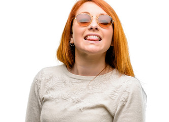 Beautiful young redhead woman sticking out tongue at camera at sign of disobedience, protest and disrespect isolated over white background