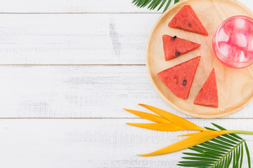 Watermelon fresh drink and watermelon on wooden plate decorate with fern leaves and bird of paradise on white wood background with copy space, selective focus on watermelon drink and ice