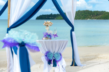 Obraz na płótnie Canvas Beautiful tropical beach with decorated wedding pergola with blue and white materials prepared for ceremony. In the centre visible table with champagne. 