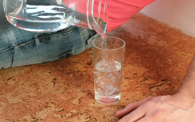 Closeup man's hand pouring a water from decanter to glass and takes a glass.