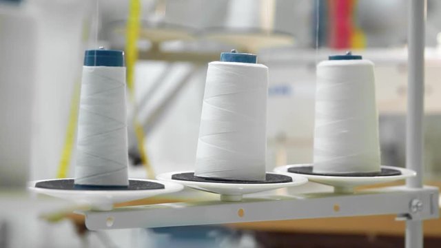 Closeup of three big bobbins with thin white thread on working professional sewing machine. Real time full hd video footage