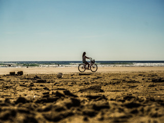Fototapeta premium woman riding bicycle on a wide beach close to the ocean during sunset