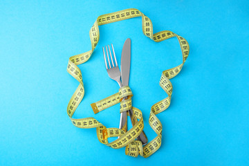 Vegetable diet for weight loss. Fork and knife are wrapped in  yellow measuring tape on blue background