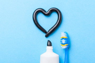 Black toothpaste from charcoal for white teeth. Tooth-paste in the form of heart, tube and toothbrush on blue background.