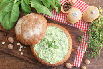 Bread loaf filled with tasty spinach sauce on table