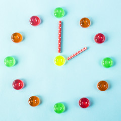 Clock lined with colorful candies on a blue background. Two hours on watch. Top view, flat lay