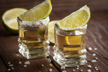 Macro photo of shots of gold Mexican tequila with lime and salt on wooden rustic background....