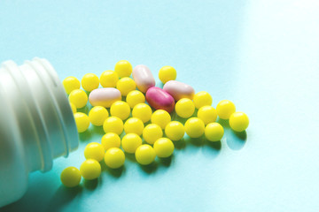 random yellow and pink pills in white bottle on blue isolated background