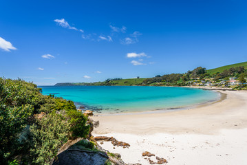 Pretty view to small paradise like town village sandy beach with turquoise blue water and red orange rocks and green shore forest on warm sunny clear sky day, Boat Harbour Beach, Tasmania, Australia