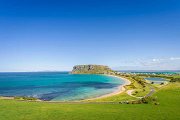 Stunning view point to big old volcanic rock mountain top called The Nut with blue turquoise water beach bay and green grass lands on warm sunny clear sky day, Stanley, North-West, Tasmania, Australia