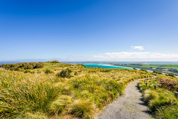 Stunning view point to big old volcanic rock mountain top called The Nut with blue turquoise water beach bay and green grass lands on warm sunny clear sky day, Stanley, North-West, Tasmania, Australia