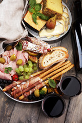 Italian antipasti wine snacks set. Cheese variety, Mediterranean olives, pickles, Prosciutto di Parma, salami and wine in glasses over black grunge background.