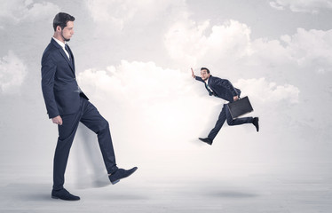 Big businessmen kicking himself as a small employee with cloudy background
