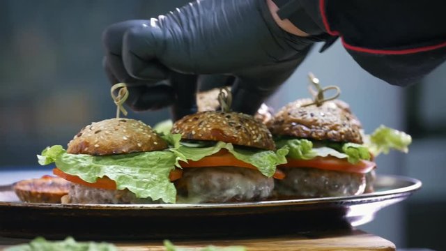 Hands of chief on commercial kitchen serves burgers on the plate - inside the restaurant