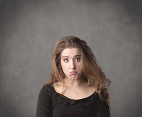 A pretty young teenage girl standing in front of a grey clear empty urban wall background concept while making funny faces.