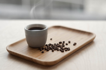 The morning hot coffee from which steam comes lies on the table next to the roasted coffee beans. Side view with copy space for your text