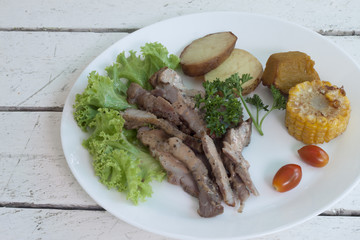 Pork steak cut into pieces on a white plate with Corn, potatoes and golden pods.