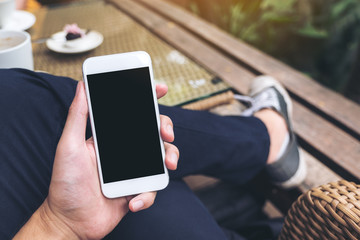 Mockup image of a man's hand holding white mobile phone with blank black screen in cafe