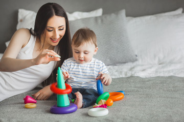 Young pretty mother playing with her little son. Cheerful family having fun indoors with little baby son